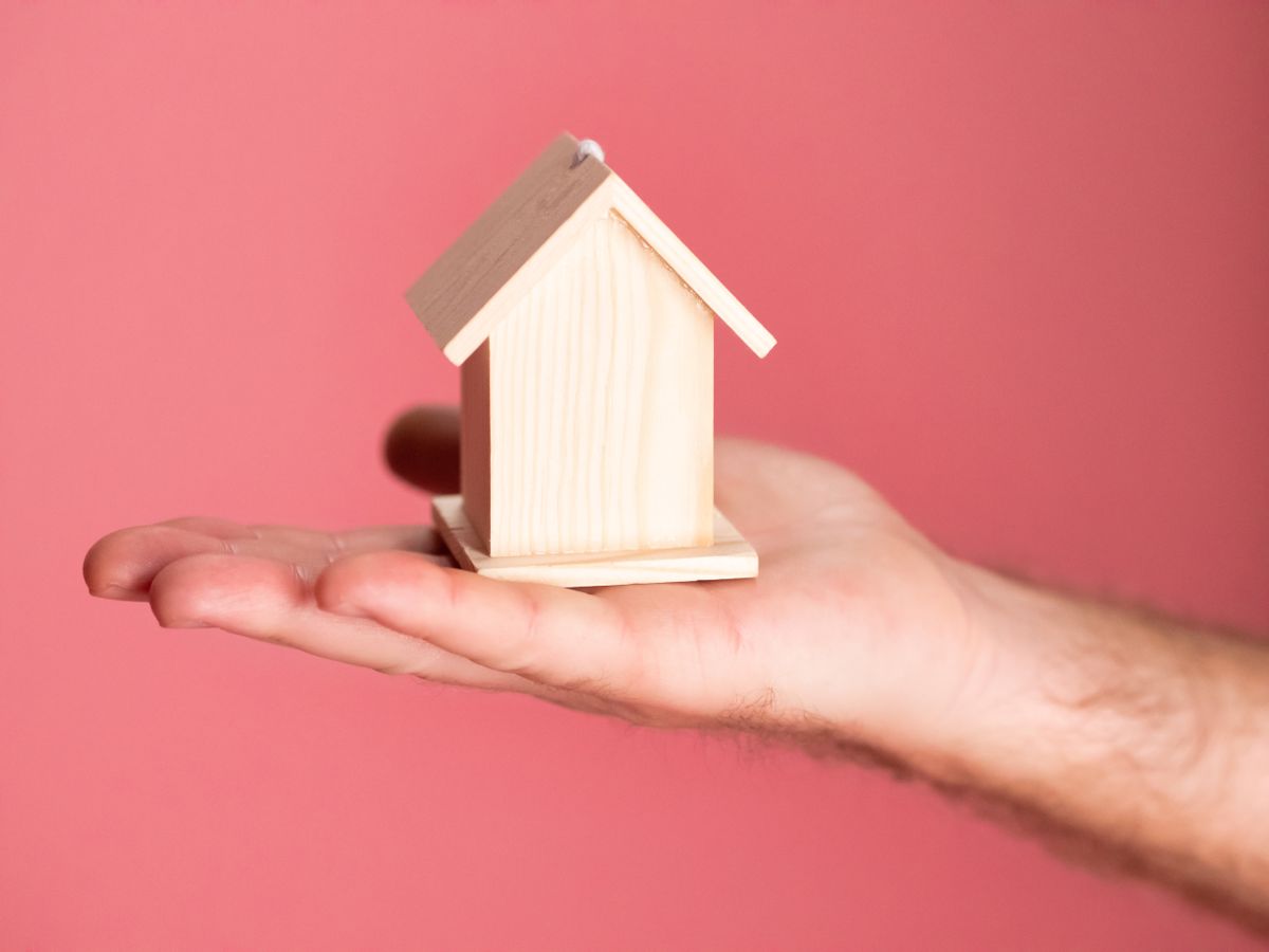 Hand holding a small model house; the credit score to buy a house
